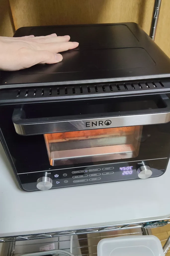 450℃で予熱中のENRO電気ピザ窯miniの本体上部に手をかざしている様子。断熱性が高く熱くならない